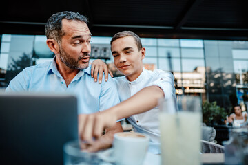 Obraz premium Handsome and happy father and his teenager son sitting in a restaurant and talking.