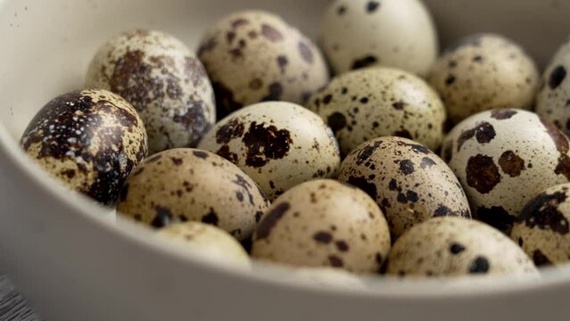 Brown spotted quail eggs in kitchen ceramic bowl. Raw farm ingredients close up. Rotation