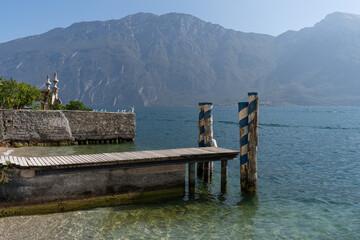 wooden jetty with mooring posts to the clear Garda  lake with a view of the rocky mountains on a sunny day