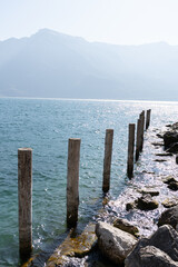 mooring posts on the embankment of a clear lake on a sunny day and mountains in the background