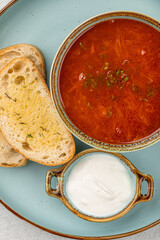 Portion of slavic traditional red sour soup borscht with toast and cream