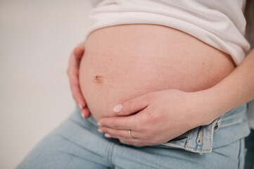 Closeup belly of a woman. Pregnancy motherhood concept. Pregnant woman. Female waiting for newborn baby. Young pregnant girl touching and holding her belly and caring about health indoors.