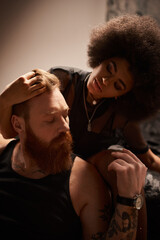 african american woman touching red hair of boyfriend with beard and tattoos in dark bedroom, desire