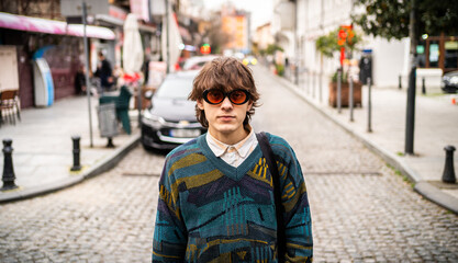 Stylish young man in vintage sweater and sunglasses on city street.