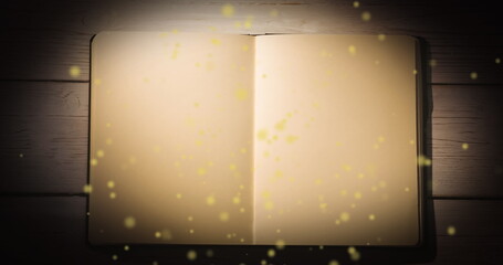 Fototapeta premium Image of yellow glowing spots over open book with copy space