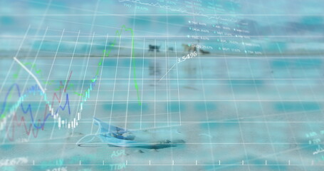 Image of trading board and graphs over close-up on mask and dogs playing on beach