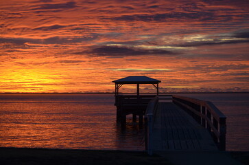 A pier in silhouette during a brilliant sunrise with the sky streaked with colors..