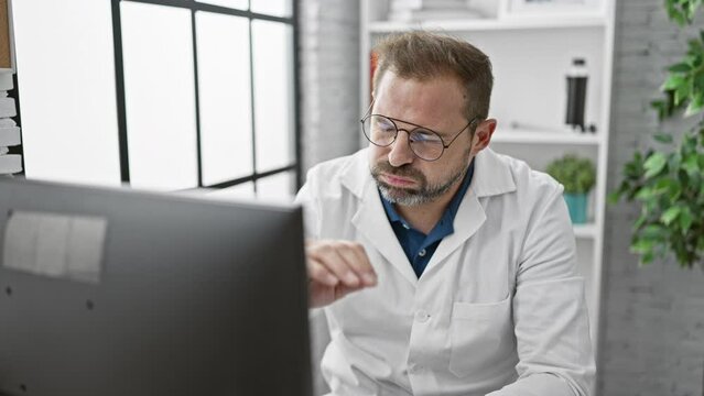 Mature man in glasses focused on screen in medical clinic office background