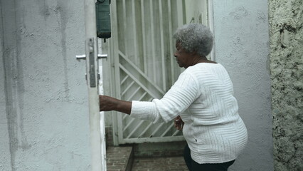 Elderly South American black woman arrives home from sidewalk street, opens residence front door...