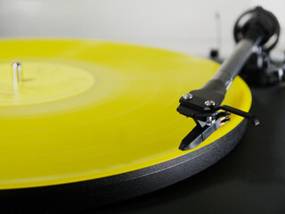 Closeup of a yellow vinyl LP record on a turntable, with the tonearm needle or stylus positioned at...