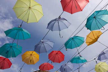 Colorful umbrellas are hanging from wire with sky background 