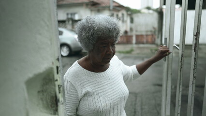 One elderly black lady opening residence front door from urban sidewalk and climbs up the stairs...