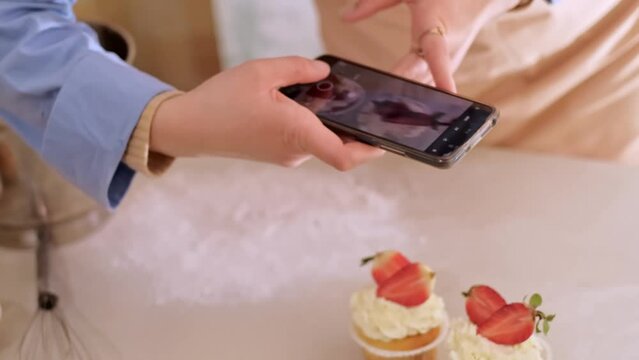 A female pastry chef takes photos with her mobile phone to advertise her website, showcasing homemade baking. Experience small-scale, eco-friendly production with gluten-free and sugar-free products