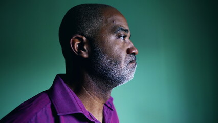 One pensive senior black man regretting past decision grimacing during challenging times standing indoors in isolation gazing at window, profile close-up face - obrazy, fototapety, plakaty