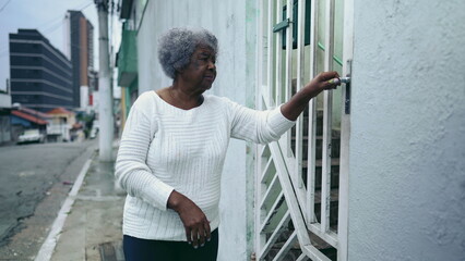 One elderly black lady opening residence front door, arriving home from urban sidewalk street. 80s...