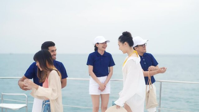 Man and woman yacht crew in uniform helping group of passenger tourist get on luxury private catamaran boat yacht to sailing in the ocean on summer holiday vacation. Cruise ship service occupation.