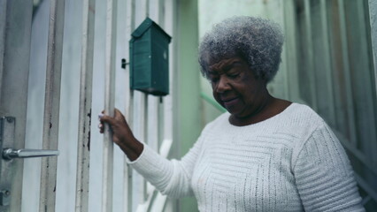 One elderly black woman from South America steps out in the street from residence front door into...