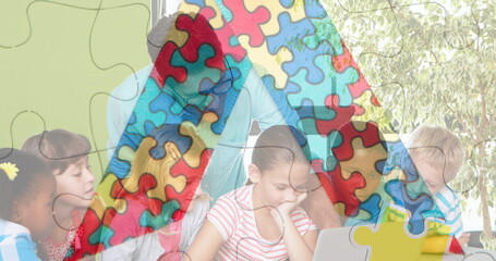 Image of puzzle pieces over diverse schoolchildren and teacher using laptop