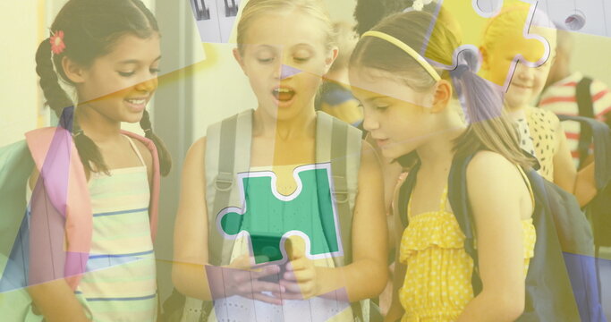 Image of puzzle pieces over diverse schoolchildren using smartphone
