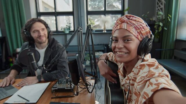 UGC POV footage of African American female guitarist talking on camera and filming blogger content after recording musical podcast with Caucasian male host in studio