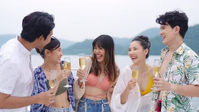 Group of Asian man and woman friends enjoy and fun luxury outdoor lifestyle celebration party drinking champagne together during travel ocean on sailing private catamaran boat yacht on summer vacation