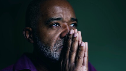Spiritual African American senior person praying to GOD, closing eyes in contemplation with hands clenched together. Faithful man asking for HELP and SUPPORT - obrazy, fototapety, plakaty