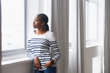 Woman, serious and thinking by window in new home with confidence for real estate investment and...