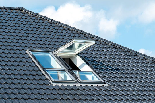 Two roof window on a grey tiled rooftop, one roof window is opened