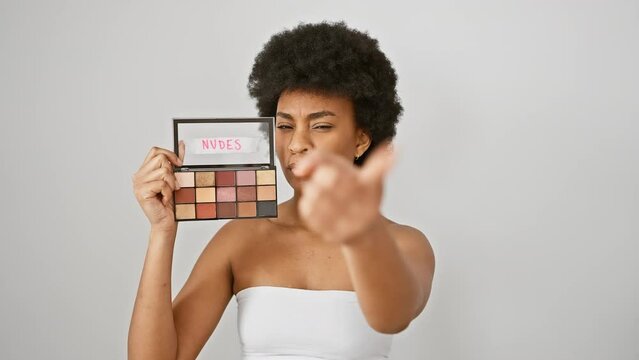 Confident, serious african american woman proudly pointing at you with makeup in hand. single adult making her point and leading the way against an isolated white wall background.