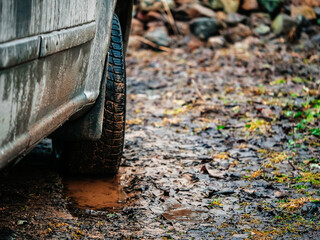 Fototapeta na wymiar Car tires in water and mud. Living on a farm far away from comfortable city life. Trip to nature in tough rough condition on 4x4 truck. Off road voyage to a forest in bad weather.