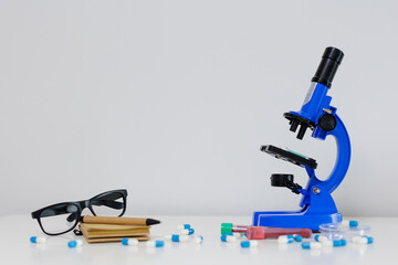 Blue microscope, eyeglasses and pills on table