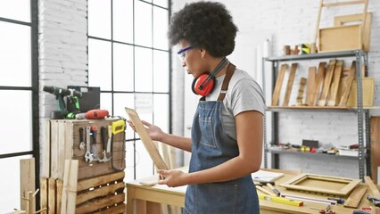 African american woman inspects wood in a well-lit carpentry workshop
