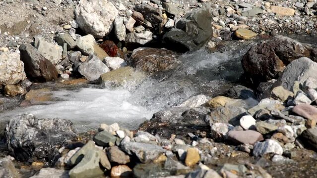 ripresa video in tempo reale, di un ruscello di montagna visto a livello del terreno e di lato, mentre l'acqua limpida e fresca scorre rapidamente tra i sassi e le rocce