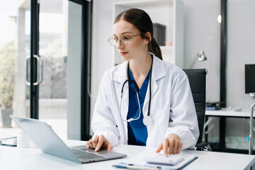 Young female doctor in white medical uniform using laptop and tablet talking video conference call at desk,Doctor sitting at desk and writing a prescription for her patient
