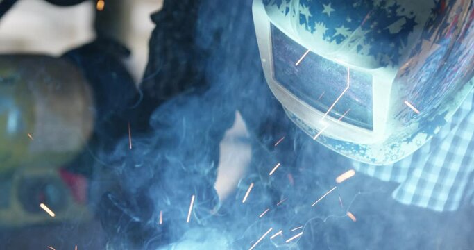 Welder with American Flag welding helmet face mask works with Mig Arc Welder to weld American Steel and throw lots of bright sparks in slow motion.