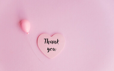 Thank you message on a pink heart sticky note on pink background 