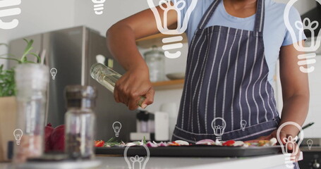 Image of lightbulbs over afrcian american woman preparing food in kitchen