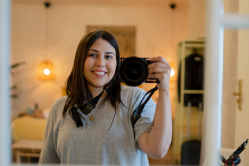 mujer haciéndose un selfie con una cámara de fotos, mujer haciéndose un selfie, mujer mirándose a un espejo, mujer sonriendo haciéndose un selfie