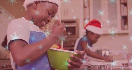 Image of snow falling over two smiling children with santa hats preparing cookies