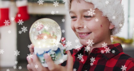 Image of snow falling at chrsitmas over happy caucasian boy with snow globe