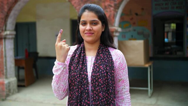 A beautiful young college student happily showing her blue mark on the index finger - general elections  a registered voter  an Indian citizen. A pretty girl posing for the camera at the voting cen...