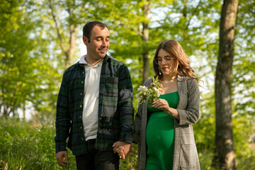 Happy couple expecting a baby spend time outdoors on a sunny day, being hugged. Walking in the park.