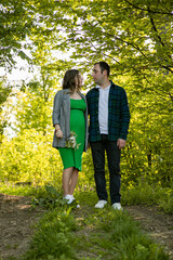 Fototapeta premium Full length image of a happy couple expecting a baby spend time outdoors on a sunny day, being hugged. Fatherhood concept.
