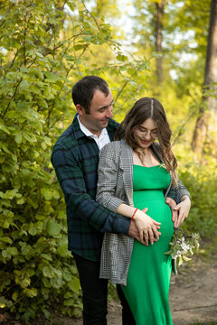 Front image of a happy couple expecting a baby spend time outdoors on a sunny day, being hugged. Vertical view.