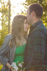 A couple expecting a baby spend time outdoors on a summer day, being hugged.