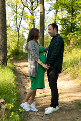 Obraz premium Full length image of a couple expecting a baby spend time outdoors on a summer day, being hugged.