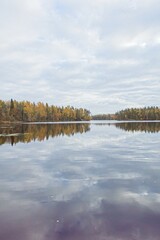 View of lake Fiskträsk with forest and cloudy sky reflecting on water surface in autumn, Sipoo, Finland.