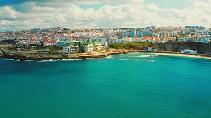 Drone is flying over ocean towards  Beautiful resort touristic town. Aerial view - Beautiful travel destination with ocean rocky shore.  Tourist place for surfing  while vacation at Ericeira, Portugal