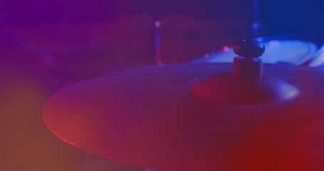 Image of hands of drummer playing drum kit, cymbal in foreground, red and blue light