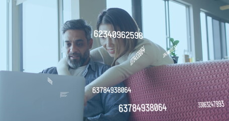 A couple is sitting in a living room using a laptop and talking
